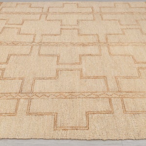 May include: A natural fiber rug with a geometric pattern in a light brown color. The rug has a woven texture and a subtle sheen.