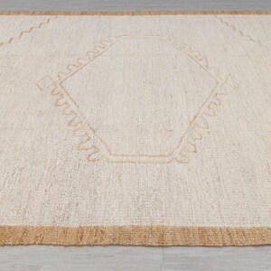 May include: A white woven rug with a tan border and a geometric design in the center.