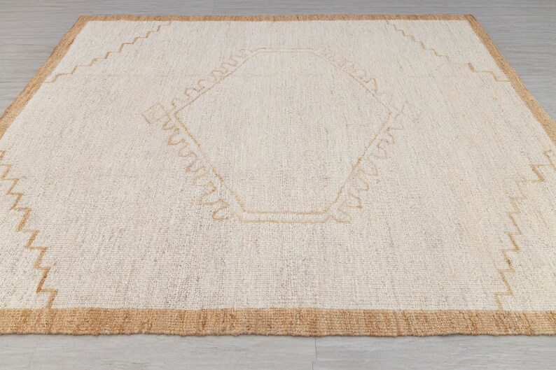 May include: A white woven rug with a tan border and a geometric design in the center.