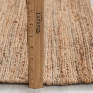 May include: Close-up of a natural fiber rug with a ruler measuring 7 inches. The rug is made of woven jute and has a natural, earthy color.