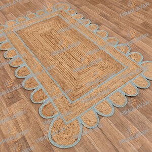 May include: A rectangular jute rug with a light blue border. The border has a scalloped edge. The rug is on a wooden floor.
