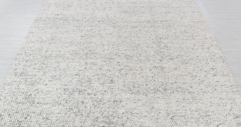 May include: A white and gray textured rug with a subtle pattern. The rug is made of a soft, woven material.