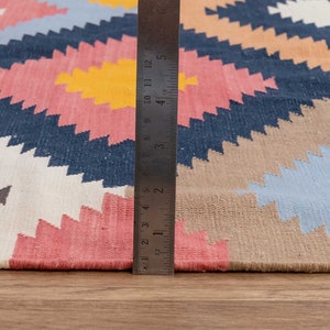 May include: A close-up of a colorful rug with a geometric pattern. A ruler is placed along the edge of the rug to show its size.