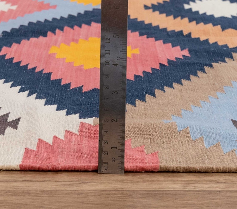 May include: A close-up of a colorful rug with a geometric pattern. A ruler is placed along the edge of the rug to show its size.