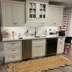 May include: A white kitchen with a bar area featuring a stainless steel sink, a wine cooler, and a white tiled backsplash. The bar area has a white countertop with a decorative rug in front of it.