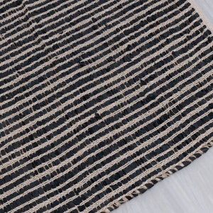 Puede incluir: Alfombra tejida negra y natural con un patr&oacute;n a rayas. La alfombra est&aacute; hecha de fibras naturales y tiene una superficie texturizada.