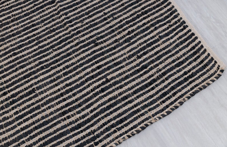 Puede incluir: Alfombra tejida negra y natural con un patr&oacute;n a rayas. La alfombra est&aacute; hecha de fibras naturales y tiene una superficie texturizada.
