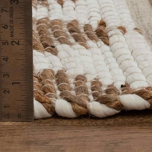 May include: Close-up of a white and brown woven rug with a fringe edge. A ruler is used to show the rug is approximately 2 inches thick.