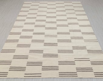 May include: A white rug with a geometric pattern of brown stripes. The rug has a simple, modern design.