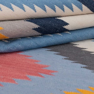 May include: A close-up of a folded woven rug with a geometric pattern in shades of blue, gray, yellow, and pink.