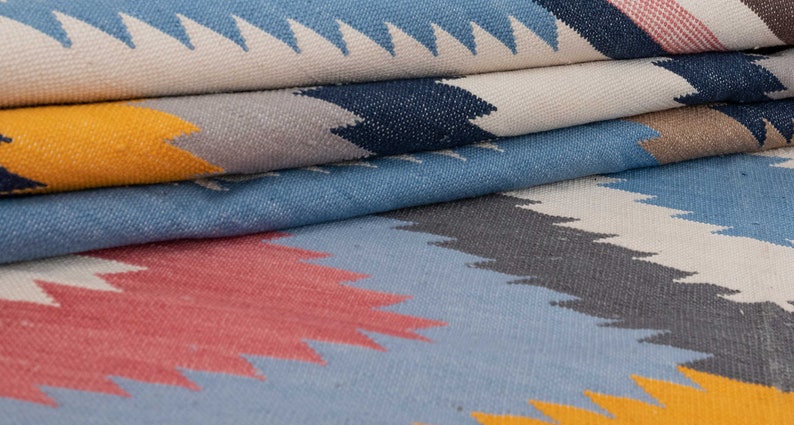 May include: A close-up of a folded woven rug with a geometric pattern in shades of blue, gray, yellow, and pink.