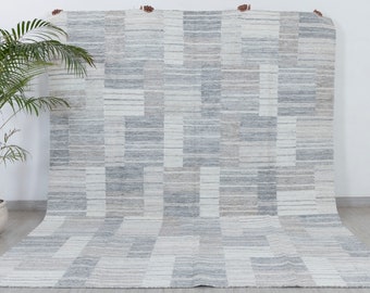 Puede incluir: Una alfombra de área contemporánea con un patrón geométrico en tonos de gris y blanco. La alfombra tiene una forma rectangular y una textura tejida.