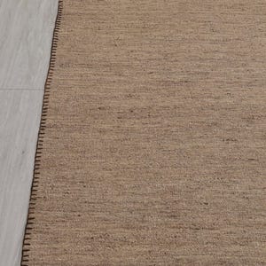 May include: A brown woven rug with a dark brown stitched border.