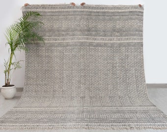 Puede incluir: Una alfombra con estampado en blanco y negro con un diseño geométrico. La alfombra tiene un borde de flecos y está hecha de fibras naturales.