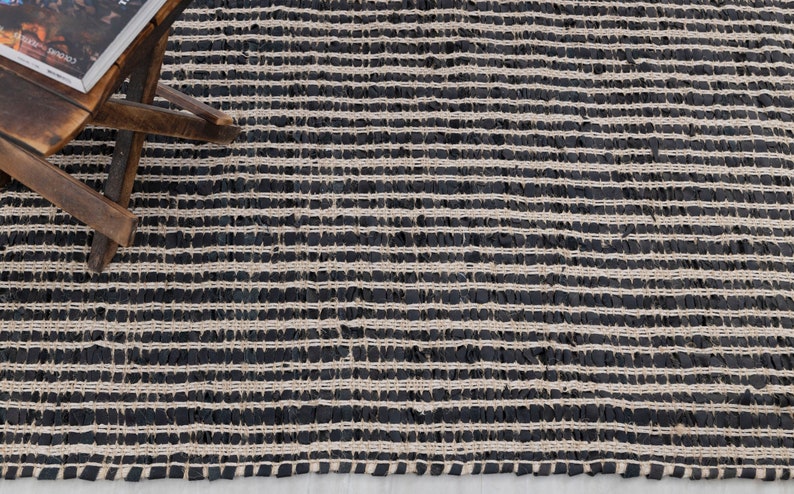 Puede incluir: Alfombra de yute negra y natural con un patr&oacute;n de rayas. La alfombra est&aacute; tejida con fibras de yute gruesas y texturizadas.