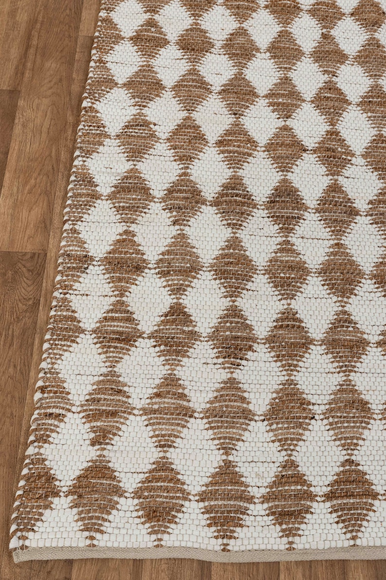 May include: A white and brown jute rug with a diamond pattern. The rug is woven with a natural fiber and has a textured surface.