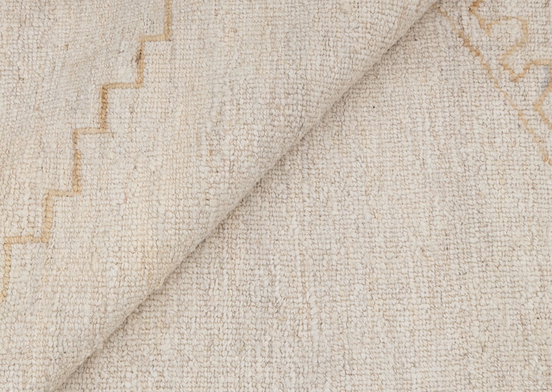May include: A close-up of a white rug with a subtle geometric pattern in a light beige color. The rug is made of a soft, textured material.