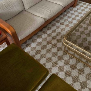 May include: A light brown and white checkered rug with a light brown couch and two green ottomans. A gold metal coffee table is on the rug.