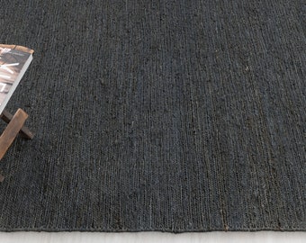 May include: A dark gray woven rug with a natural, textured surface. The rug is made of jute fibers and has a subtle sheen.