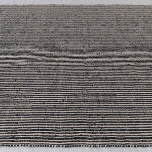 Puede incluir: Una alfombra de yute natural y negro con un patr&oacute;n de rayas. La alfombra est&aacute; hecha de fibras naturales y tiene una textura tejida.