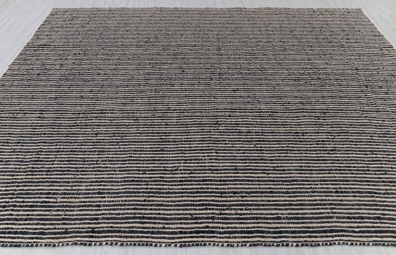 Puede incluir: Una alfombra de yute natural y negro con un patr&oacute;n de rayas. La alfombra est&aacute; hecha de fibras naturales y tiene una textura tejida.