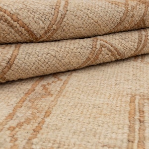 May include: A close-up of a beige and brown woven rug with a geometric pattern. The rug is folded in half, showing the texture and detail of the weave.