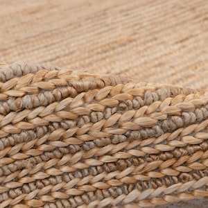 以下が含まれることがあります： 編み込まれたテクスチャを持つ天然繊維の敷物のクローズアップ。敷物は薄い茶色で、わずかに光沢があります。