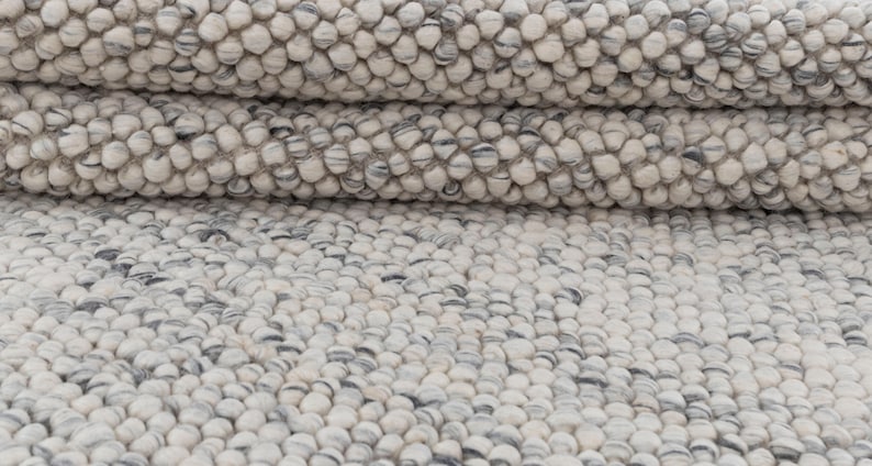 May include: A close-up of a white and gray wool rug with a textured, pebble-like surface.