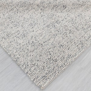 May include: A close-up of a white and gray textured rug with a subtle pattern. The rug is made of a soft, fluffy material and has a modern, minimalist design.