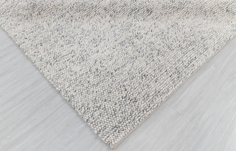 May include: A close-up of a white and gray textured rug with a subtle pattern. The rug is made of a soft, fluffy material and has a modern, minimalist design.