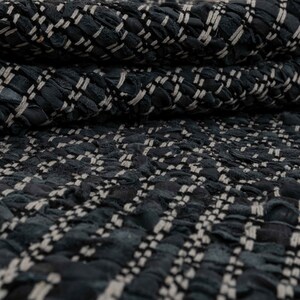 Op de afbeelding: Close-up van een zwarte en witte tweed stof met een textuur, geweven patroon.