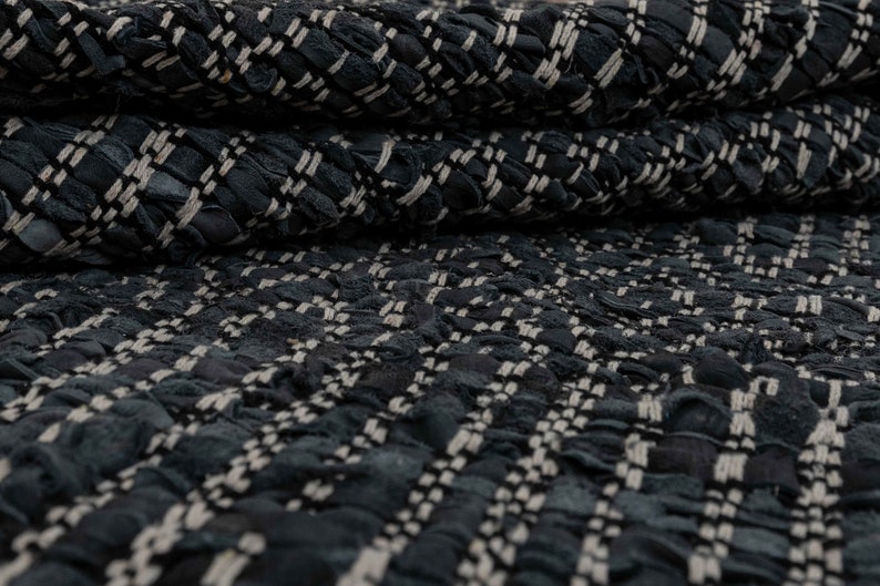 Op de afbeelding: Close-up van een zwarte en witte tweed stof met een textuur, geweven patroon.