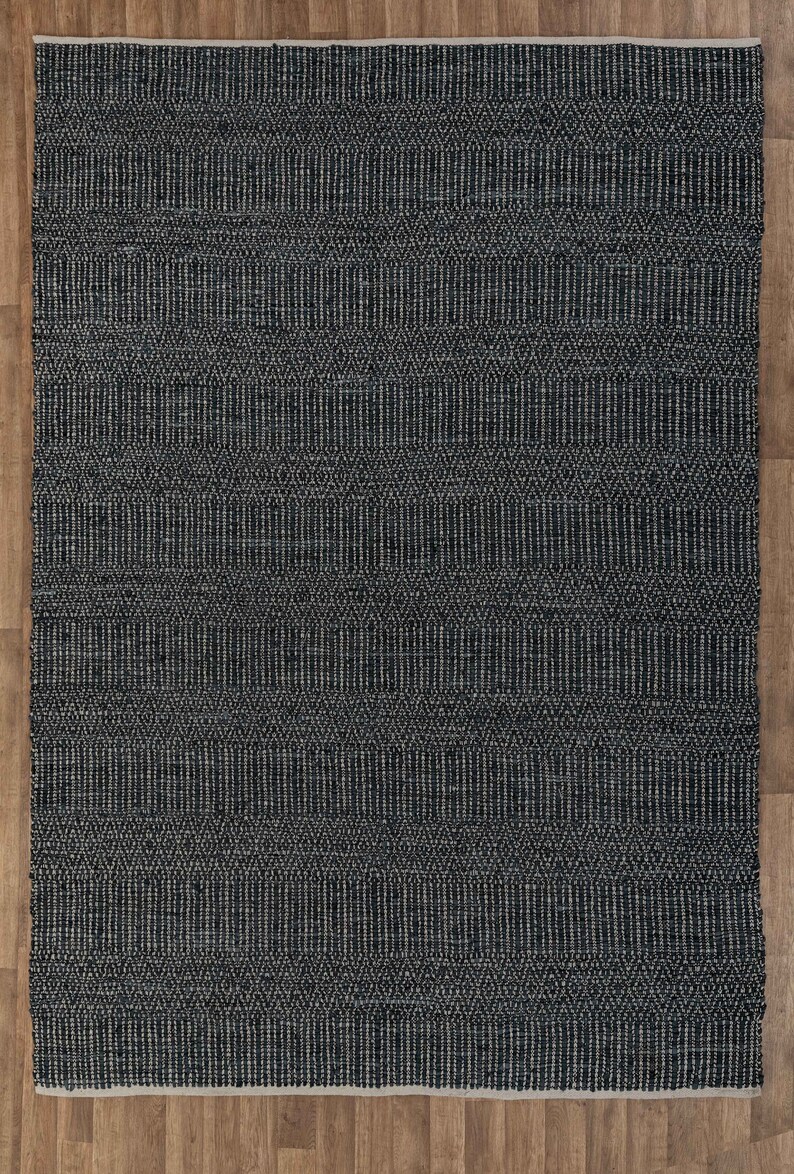 Op de afbeelding: Een zwart-wit geometrisch patroon tapijt met een geweven textuur. Het tapijt heeft een subtiele glans en is gemaakt van natuurlijke vezels.