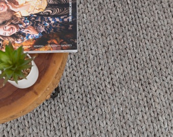 May include: A close-up of a gray braided rug with a wooden table and a potted plant on top. The table has a magazine on it with the text "The Forecast" and "Colours - Textures - Fashion".