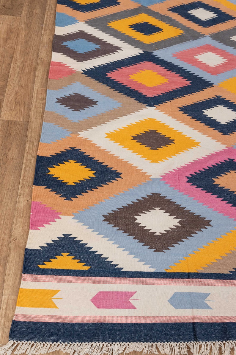 May include: A colorful rug with a geometric pattern in shades of blue, pink, yellow, and brown. The rug has a fringe border.