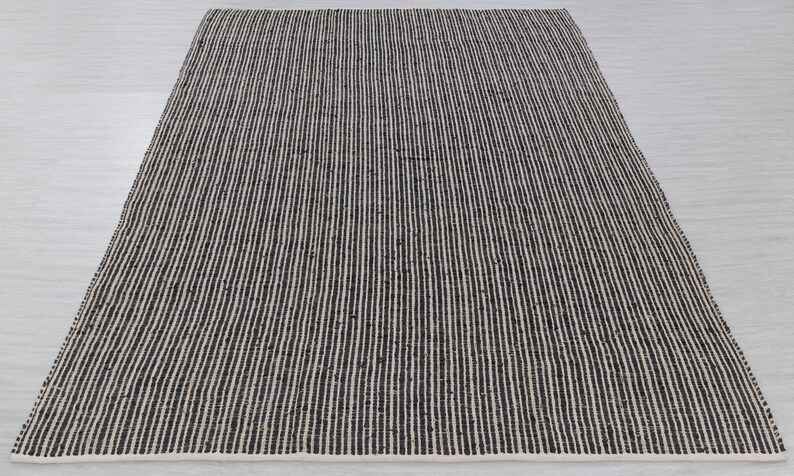 Puede incluir: Una alfombra rayada en blanco y negro hecha de fibras naturales. La alfombra tiene una textura tejida y un dise&ntilde;o simple.