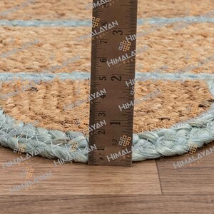 May include: Close-up of a blue and brown jute rug with a scalloped edge. A ruler is placed along the edge of the rug to show the size.