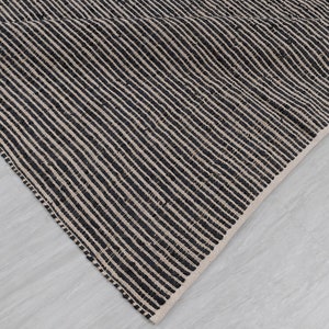 Puede incluir: Primer plano de una alfombra rayada en blanco y negro con un tejido texturizado. La alfombra est&aacute; doblada sobre s&iacute; misma, mostrando el rev&eacute;s de la tela.