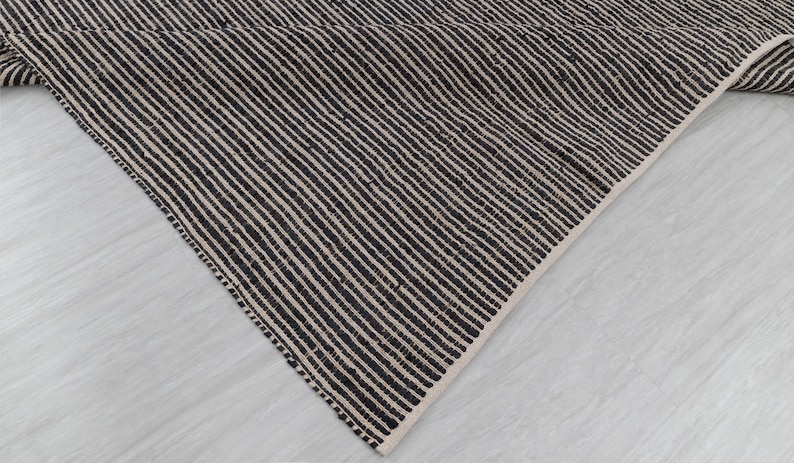 Puede incluir: Primer plano de una alfombra rayada en blanco y negro con un tejido texturizado. La alfombra est&aacute; doblada sobre s&iacute; misma, mostrando el rev&eacute;s de la tela.