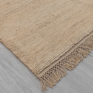 May include: A beige rug with a fringe border. The rug is made from a natural fibre and has a textured surface.