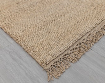 May include: A beige rug with a fringe border. The rug is made of a natural fiber and has a textured surface.