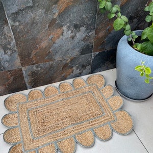 May include: A natural fiber doormat with a scalloped edge and a light blue trim. The mat is made of woven jute and is perfect for adding a touch of rustic charm to any entryway.