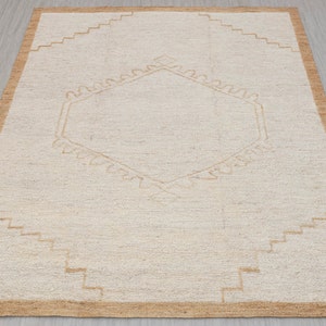 May include: A beige rug with a geometric pattern in a lighter beige color. The rug has a brown border.