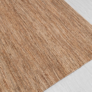 May include: A close-up of a natural fiber rug with a woven texture. The rug is a light brown color and has a subtle sheen.
