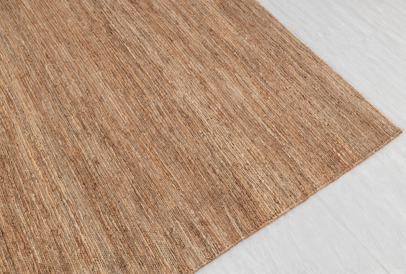 May include: A close-up of a natural fiber rug with a woven texture. The rug is a light brown color and has a subtle sheen.