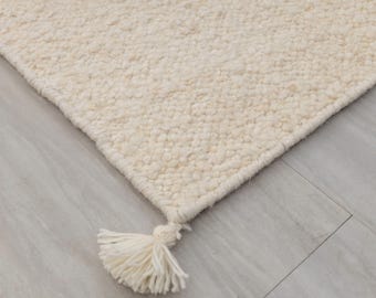 May include: Close-up of a white, fluffy rug with a fringe detail. The rug is made of a soft, textured material and has a subtle sheen.