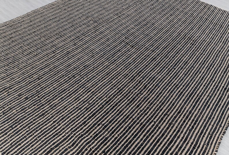 Puede incluir: Una alfombra de yute natural y negro con un patr&oacute;n de rayas. La alfombra est&aacute; hecha de fibras naturales y tiene una superficie texturizada.