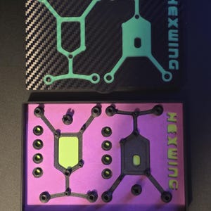 May include: Two rectangular cases labeled HEXWING. The top case has a black carbon fiber pattern lid with a light green geometric frame. The bottom case is open, revealing a bright purple interior containing black components and a light green insert.