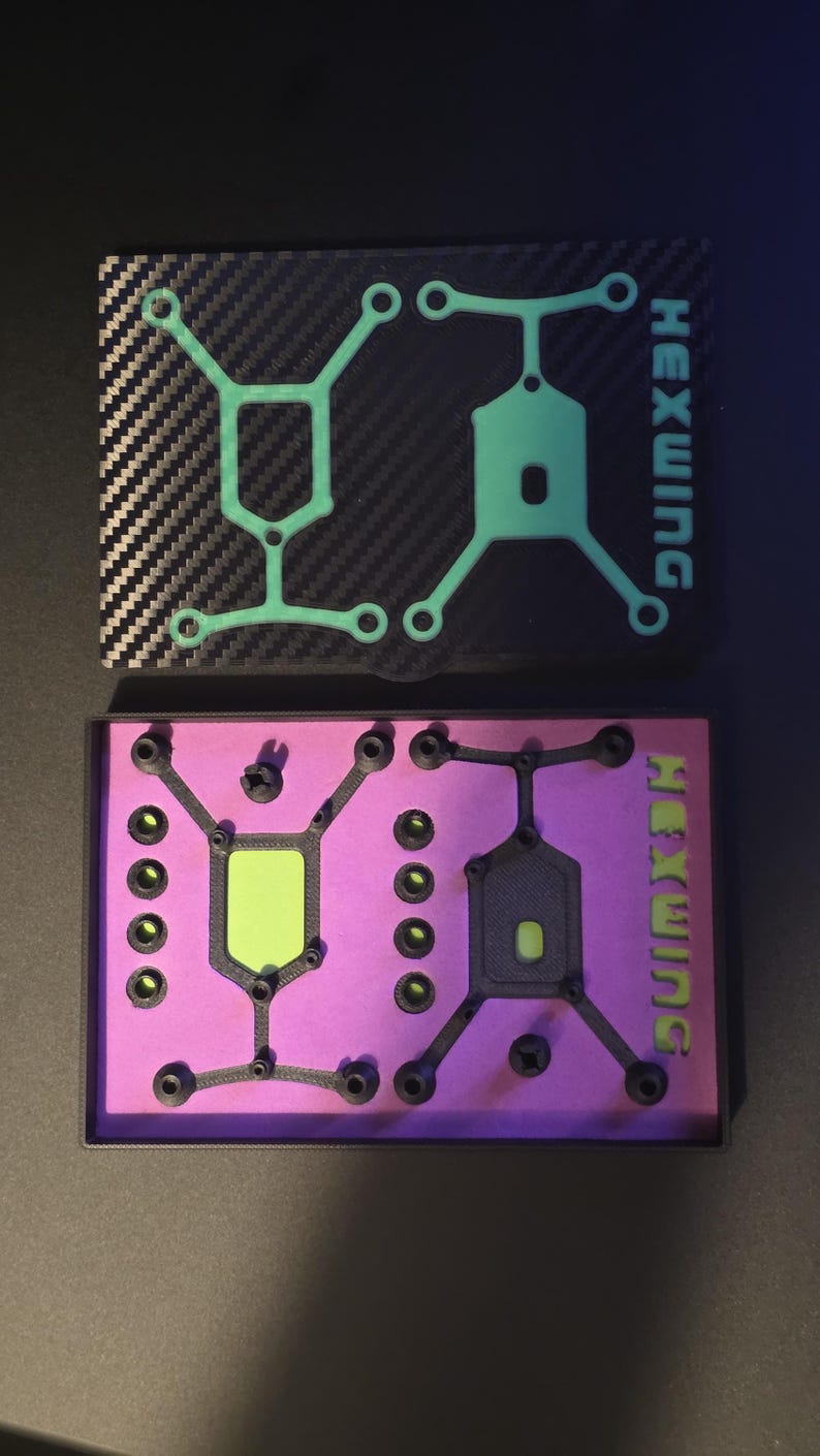 May include: Two rectangular cases labeled HEXWING. The top case has a black carbon fiber pattern lid with a light green geometric frame. The bottom case is open, revealing a bright purple interior containing black components and a light green insert.