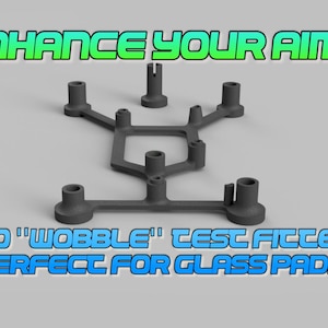 May include: A dark gray, multi-pronged plastic frame with several cylindrical mounting points. The text ENHANCE YOUR AIM + appears at the top, and the text NO "WOBBLE" TEST FITTED PERFECT FOR GLASS PADS appears at the bottom of the image.